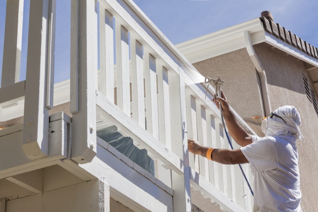 A painter uses a sprayer to paint a balcony railing, image for the blog The Foundational Approach to Property Improvements.