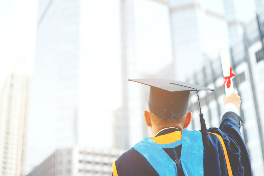Image of a recent college graduate lifting his diploma in a salute to the city skyline in the background, an image for the apartment management companies guide to renting to college grads.
